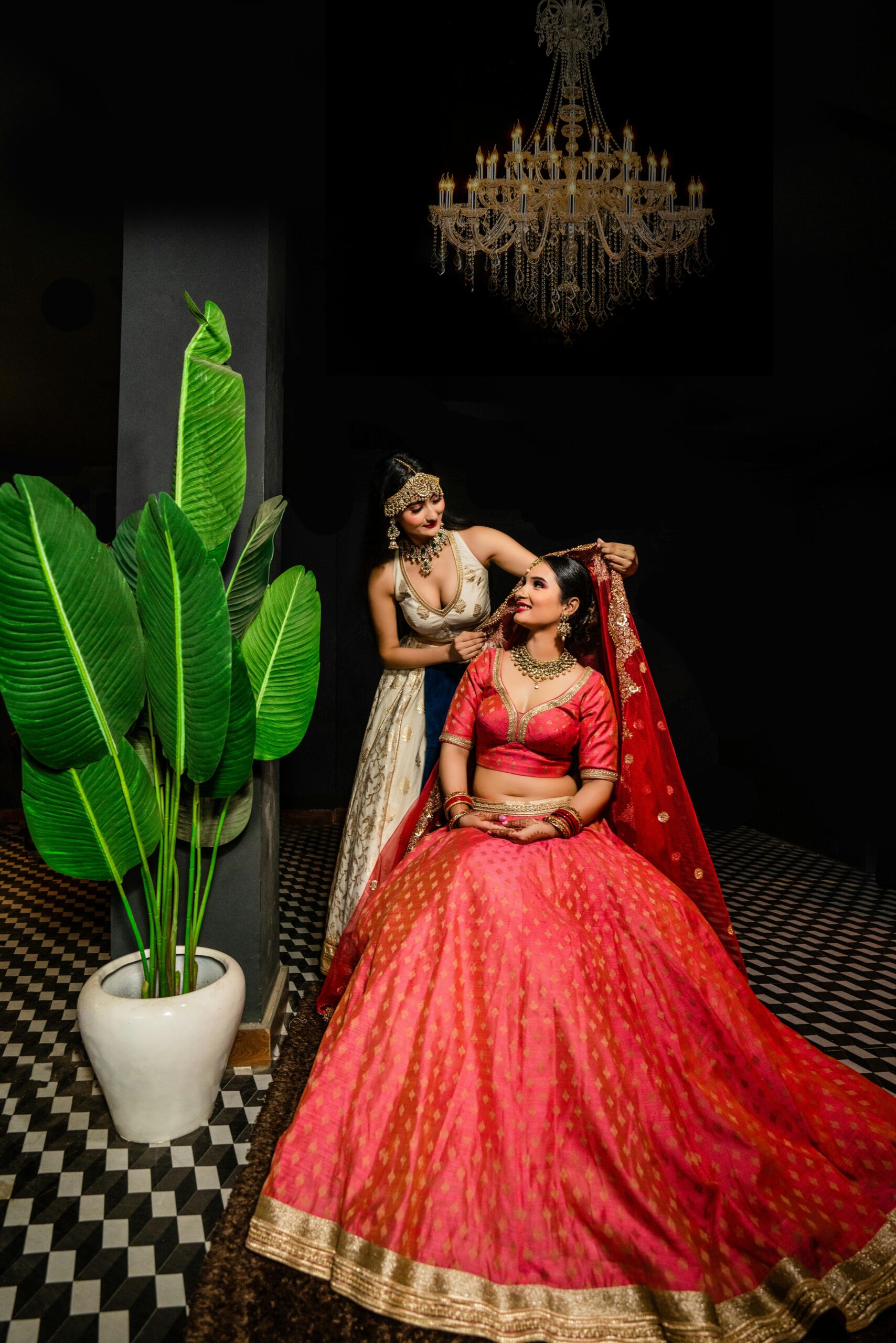Two women in vibrant traditional clothing indoors with chandelier.